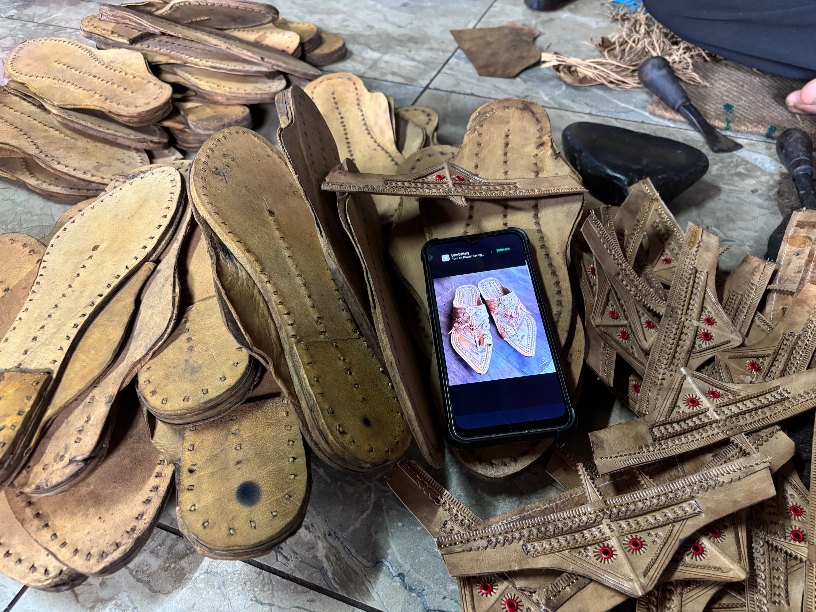 Bare sandal soles at a workshop in Kolhapur district’s Karlee village. The workshop owner displays a sample of the finished chappal on his mobile phone. Bare sandal soles at a workshop in Kolhapur district’s Karlee village. The workshop owner displays a sample of the finished chappal on his mobile phone.